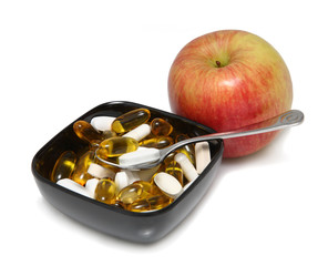 Red Fujiapple with pills in black bowl on white background