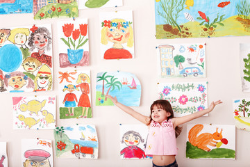 Child with hand up and picture  in playroom.