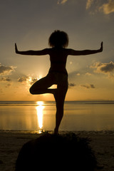 A silhouette of a woman facing the sunset in a yoga pose