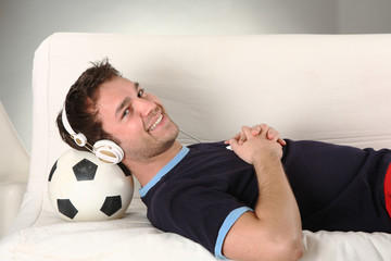 junger mann mit kopfhörern hört musik und liegt auf fussball