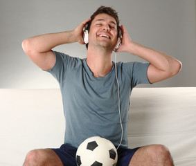 junger mann mit kopfhörern hört musik und hat einen fussball