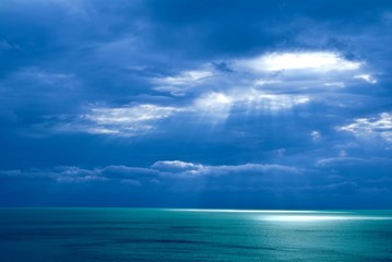 Naklejka na ściany i meble sunlight pushing through a clouds above a sea