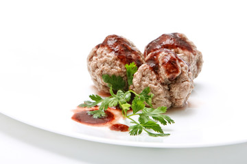 Boiled meatballs with gravy and parsley on white background