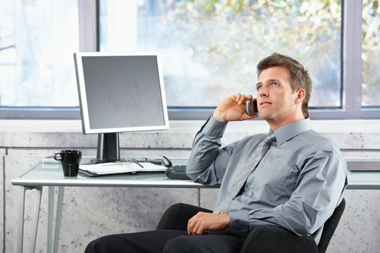 Businessman on call sitting at desk looking up