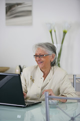 Femme senior souriante assise devant ordinateur portable