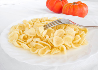 Orecchiette on white dish with fork and tomatoes in background.
