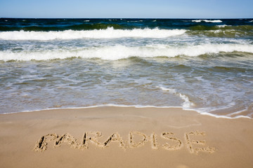 Paradise written in sandy beach