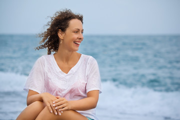 Curly beautiful young woman sitting near sea in evening