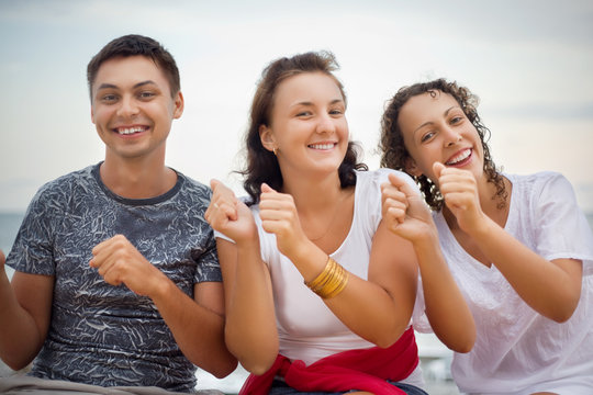 Smiling man and two young women dancing sitting on beach