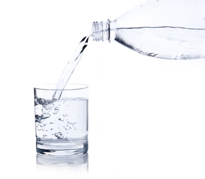 Water, flows from a plastic bottle in a glass isolated on white