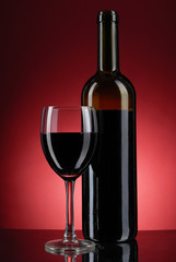 Glass of wine and bottle on red background .