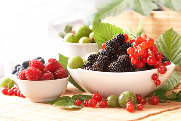 Berries in plates, on a table, among green leaves