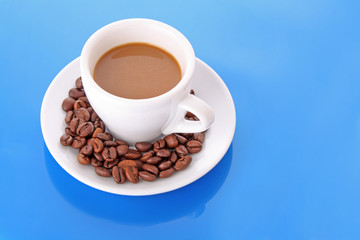 Small white   cup of coffee with coffee grain   on blue backgrou