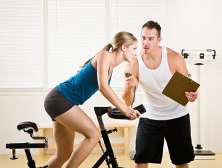 Trainer timing woman on stationary bicycle