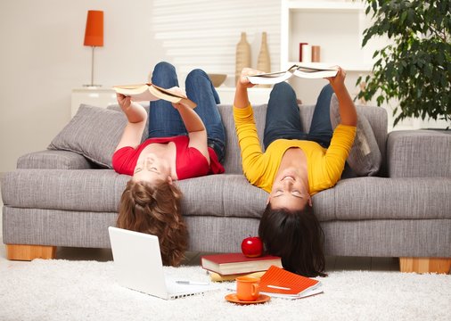 Girls reading upside down on sofa