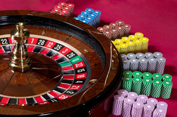 Roulette wheel and chips over a pink table.