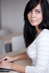 Naklejka premium pretty young brunette working/typing on a laptop computer in a o