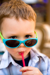 A boy with sunglasses drinking from a straw