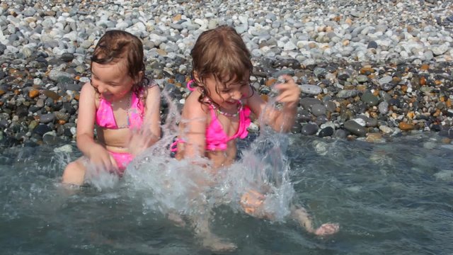 girls lying on beach with sea surf and playing with water