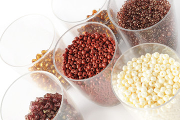 beige and brown beads in small plastic jars isolated on white