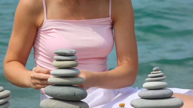 headless woman building stone stack on pebble beach