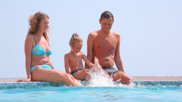 family sitting on edge of pool and shaking water by legs