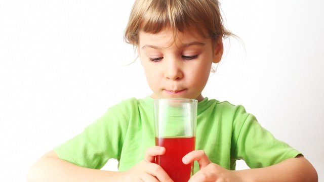 small girl holds in hands glass of juice, drink it and smiles