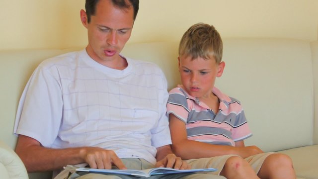 father with little son sits on divan reads children's book