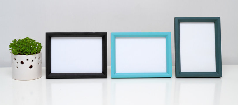 Picture frames and potted plant on white table.