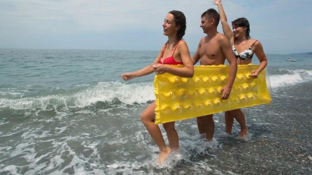 two womans and man holds inflatable mattress walking on beach