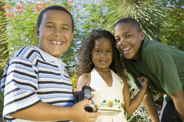boy (7-9) holding camcorder with younger sister (5-6) and older brother (10-12) portrait.