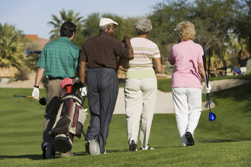 group of senior golfers walking on golf course back view