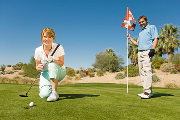 Obraz premium golfing couple watching ball roll towards golf cup