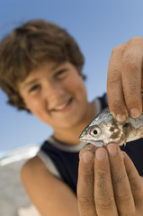 pre-teen boy holding fish on beach focus on foreground