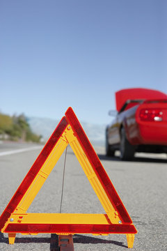 Warning Triangle In Front Of Broken Down Red Sports Car At Side Of Road