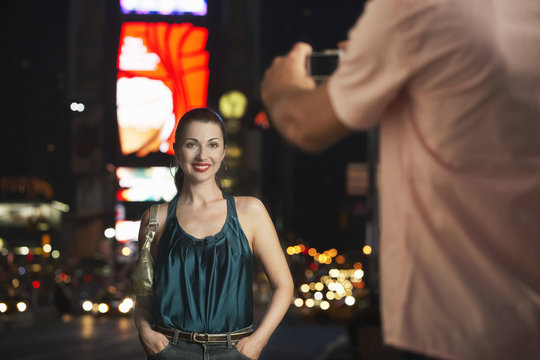 man  photographing elegant woman in times square at night