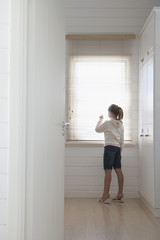 Fototapeta na wymiar young girl peering through blinds standing at window full length