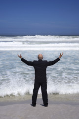 business man standing on edge of sea arms outstretched back view