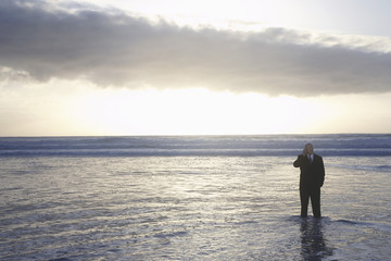 business man using mobile phone standing in sea at sunset elevated view