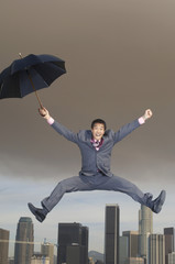 Fototapeta na wymiar business man jumping mid-air with umbrella above city