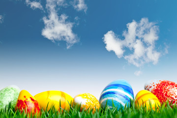 Easter eggs in green grass over blue sky with clouds
