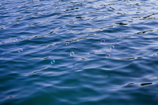 Mehrere schillernde Seifenblasen schweben &uuml;ber kaltes Wasser