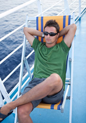 Young man resting on a deckchair while traveling on a liner acro - obrazy, fototapety, plakaty