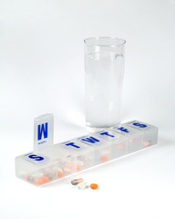 Weekly pill box with pills and glass of water