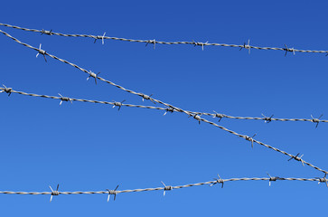 Barbed wire security fence close up and blue sky.