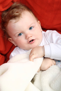 Baby girl lying on red sofa holding white blanket
