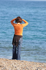 Die Frau am Meer. Eine Urlauberin steht am Wasser und schaut auf das Meer.