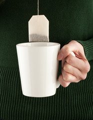 female hands holding a teacup and teabag