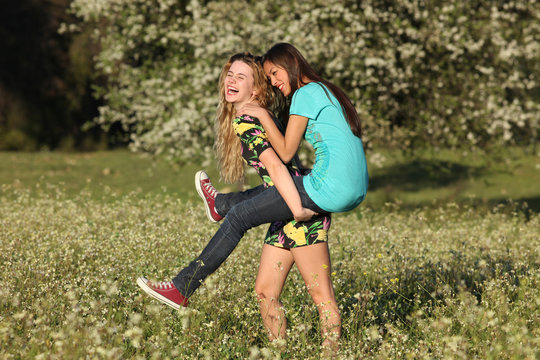 Two beautiful young women piggy- backing in blooming meadow