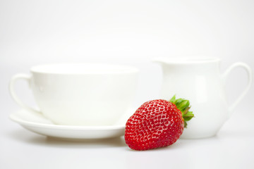 white cup and milk jug with strawberries isolated on white